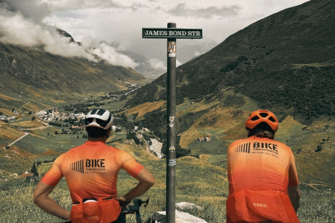 Two Bike Tour Evolution cyclists standing under the James Bond Strasse sign on the Furka Pass